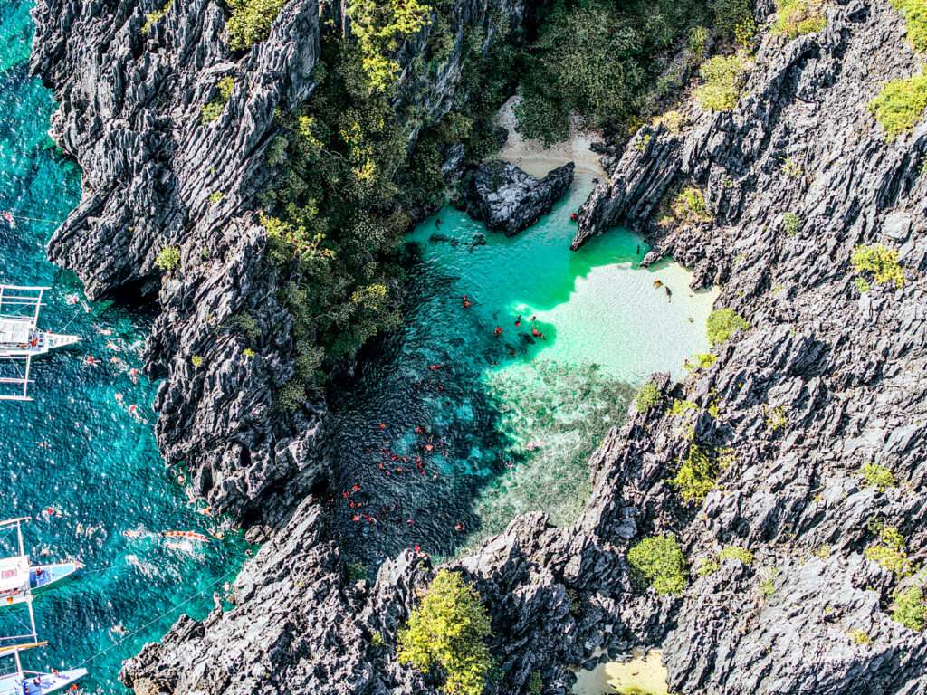 Swimmers entering Secret Beach through a narrow rock opening, El Nido